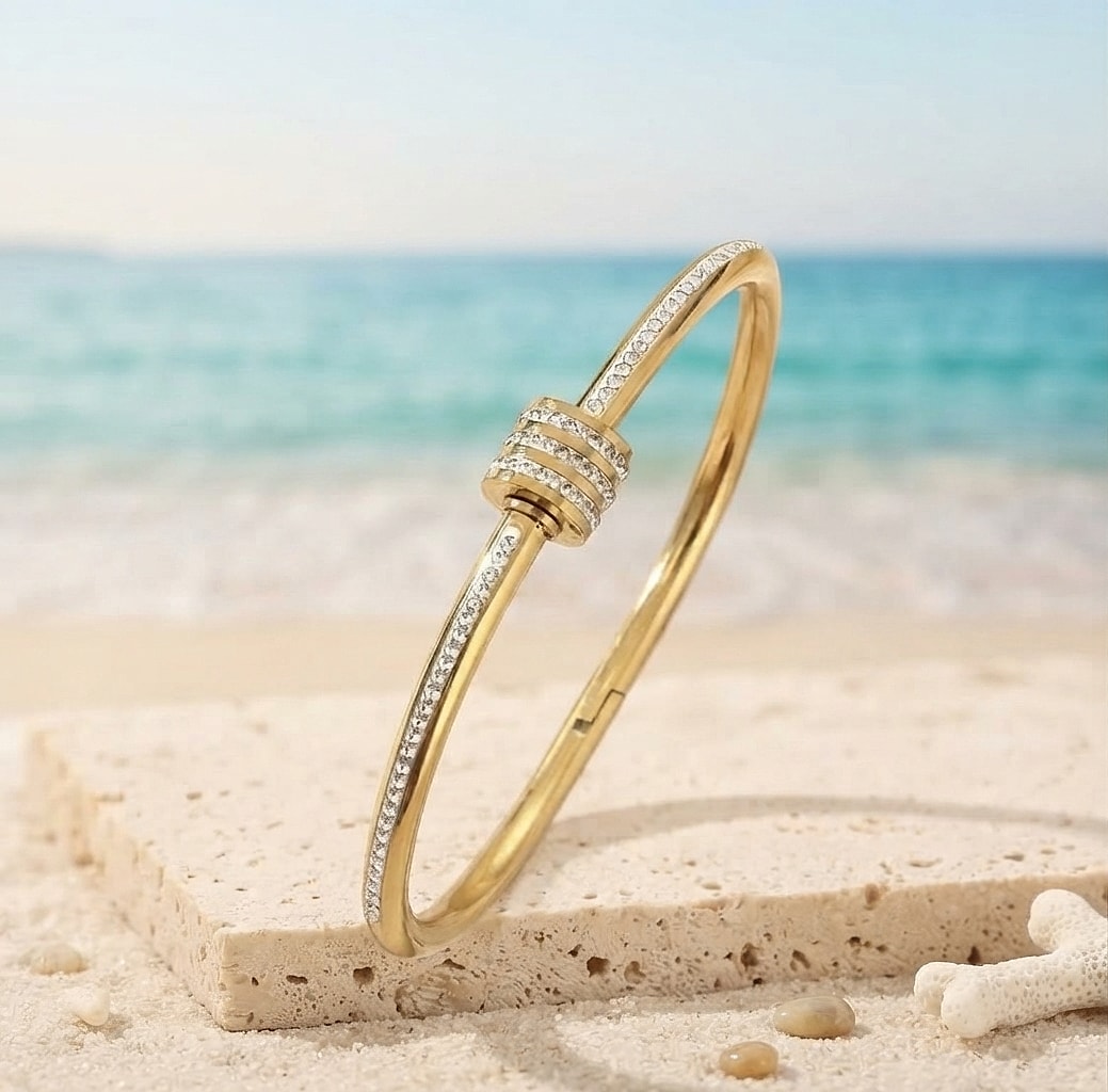 Gold zirconia bangle with screw detail on a white stone at the beach