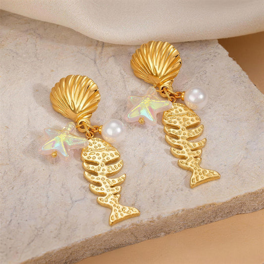 Gold shell and fish drop earrings on textured stone