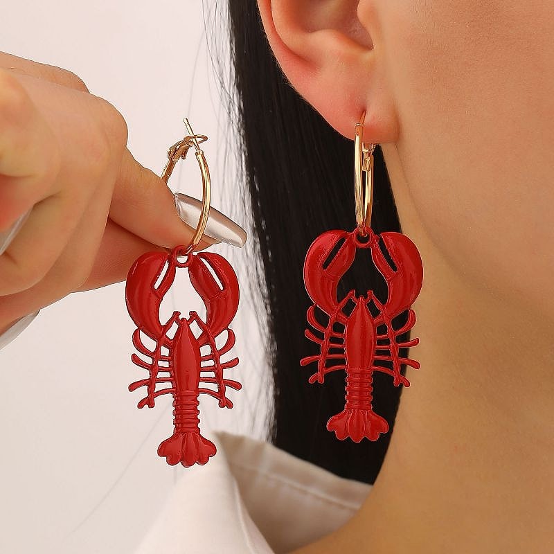 Red enamel lobster hoop earrings held up beside the ear
