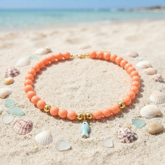 Soft coral-peach beaded necklace with a light blue ceramic fish charm