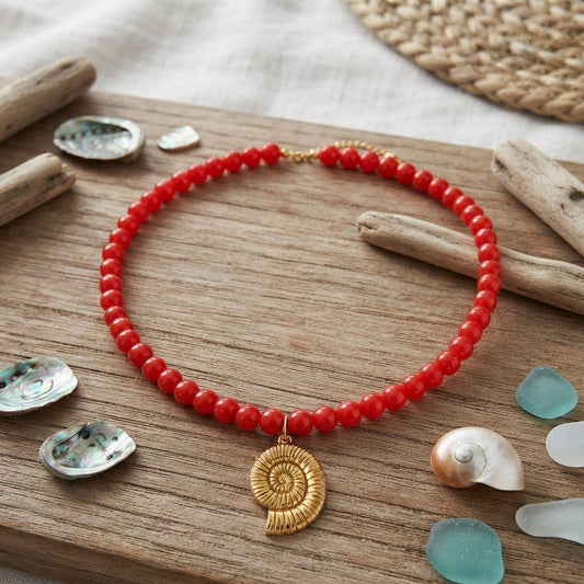 Red beaded necklace with a gold spiral shell charm