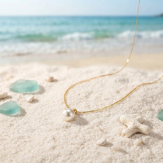 Small single pearl necklace on a hammered gold chain laid on sand