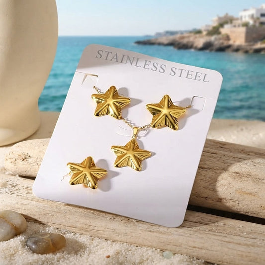 Classic gold star earrings, necklace and ring set on a card by the sea